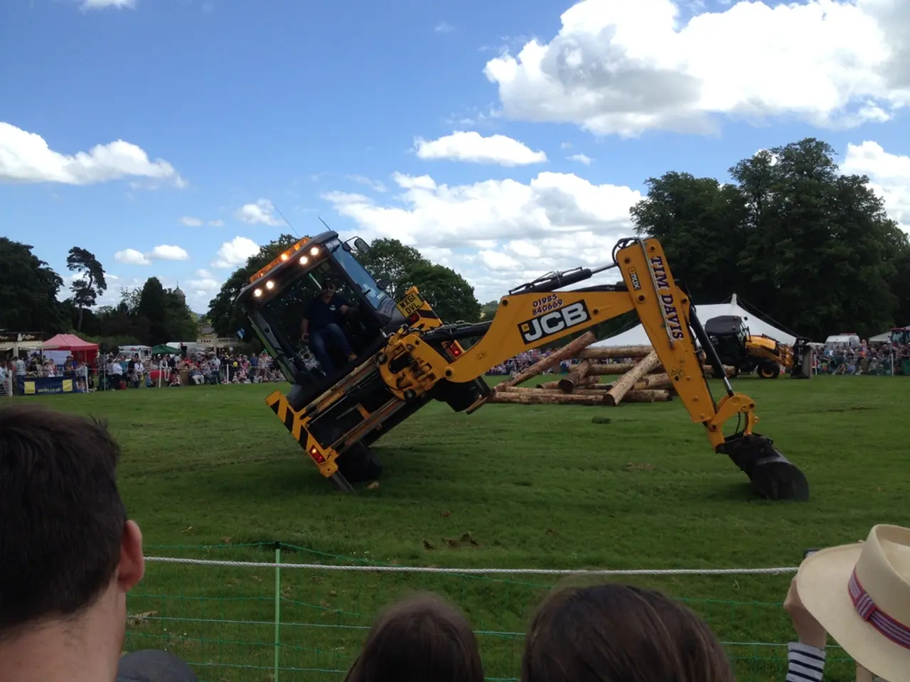 There is a JCB and a person is sitting on that. There are lights for the JCB. It is on a grass...