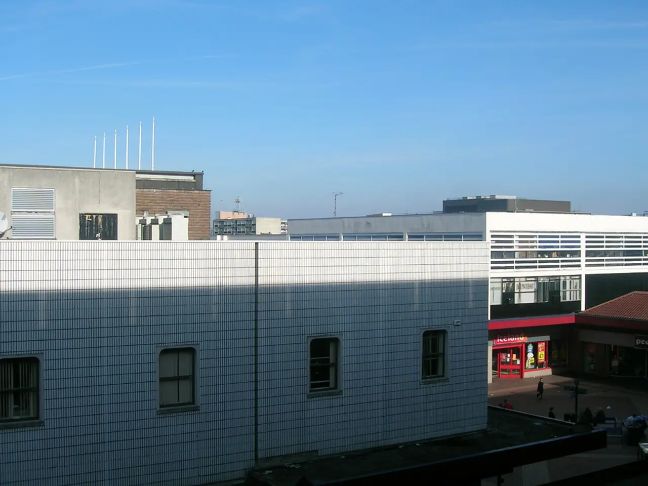 In the image there are buildings and stores and in between the buildings there are few people.