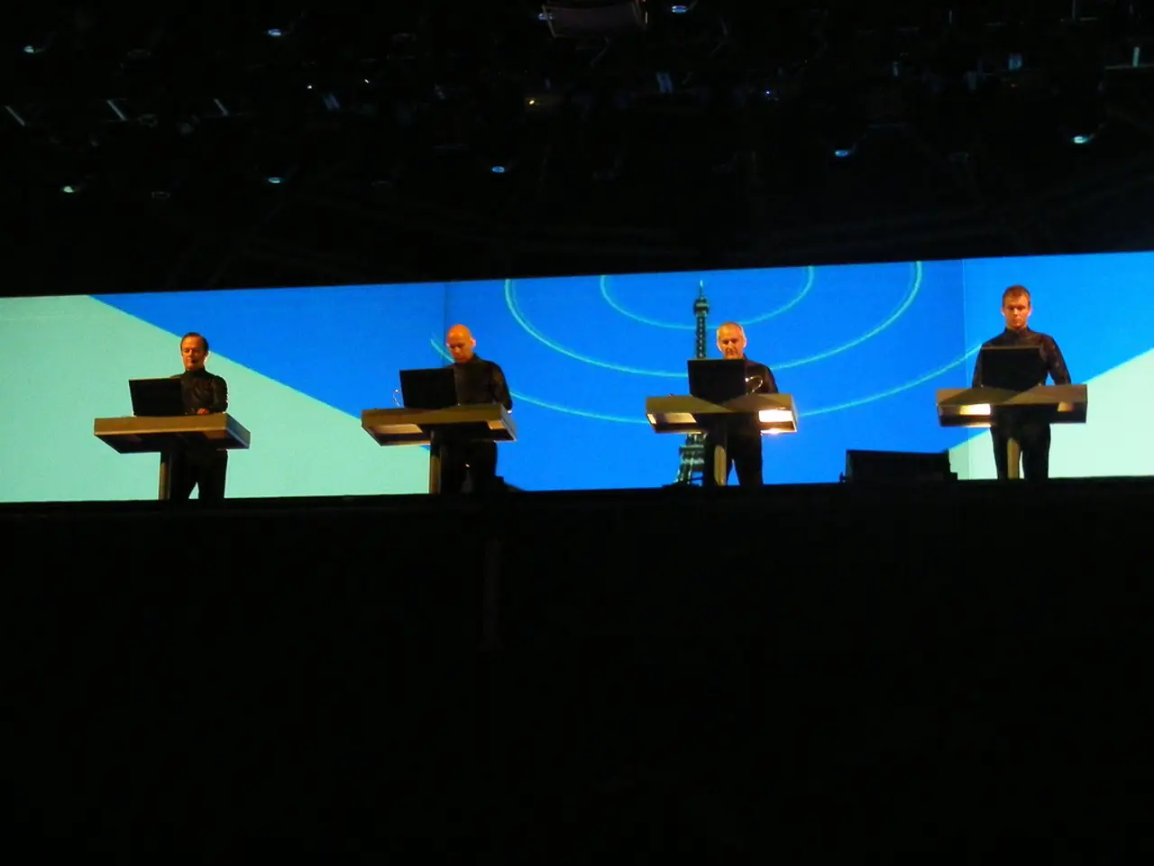 Here we can see four men standing at the podium. On each podium we can see a laptop. In the...