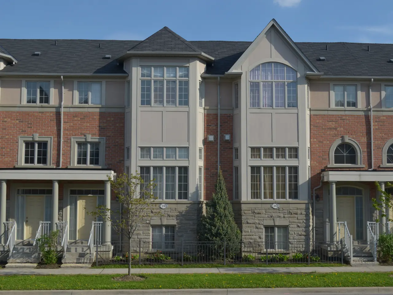 The image shows a row of townhouses in a residential neighborhood, with windows, doors, pillars,...