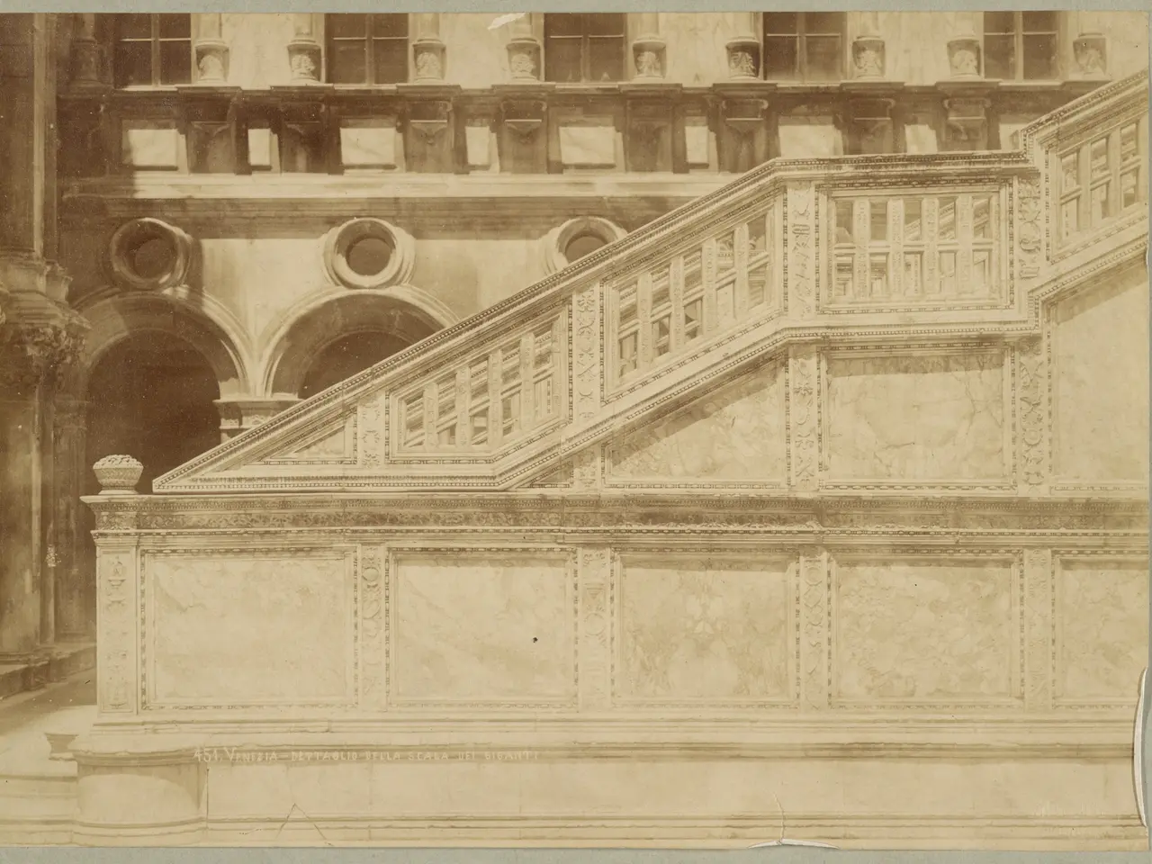 The image shows an old photo of a building with a staircase, railings, pillars, arches, and...