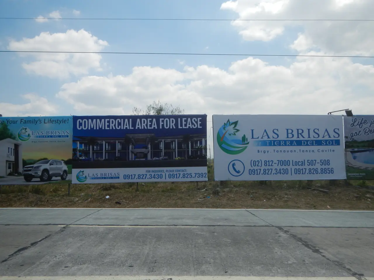 The image shows a commercial area for lease in Las Brisas, with hoardings on the road, grass,...