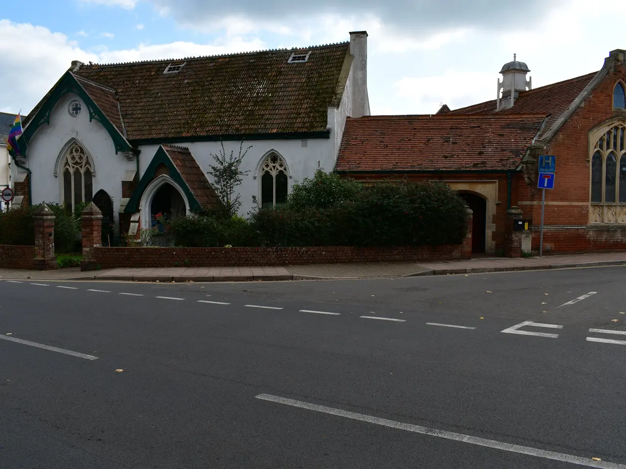 The image shows an old church on the corner of a street, surrounded by houses with roofs and...