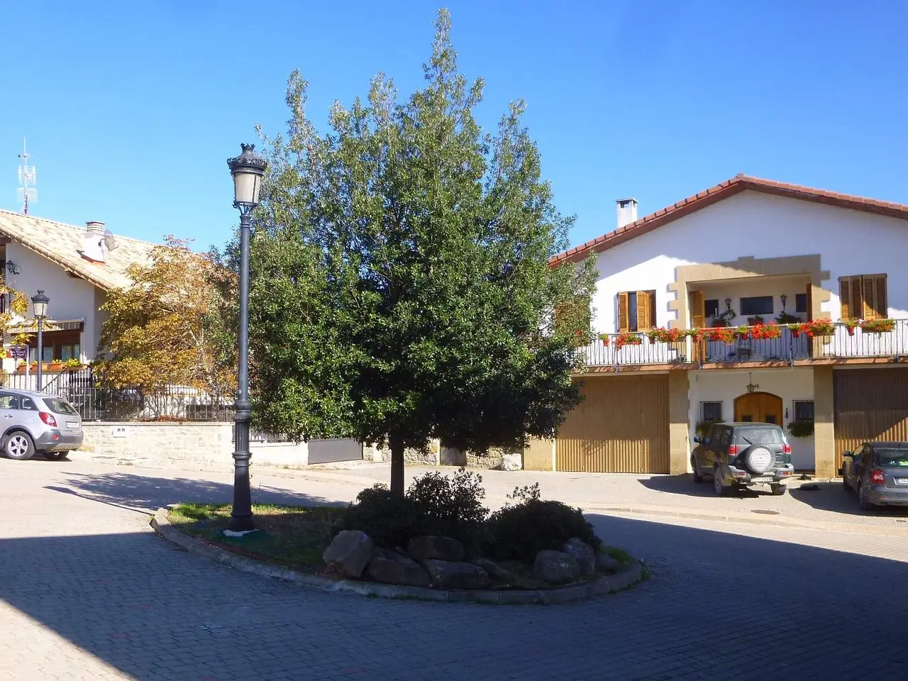 The image shows a street with cars parked in front of a building with windows, railings, doors and...