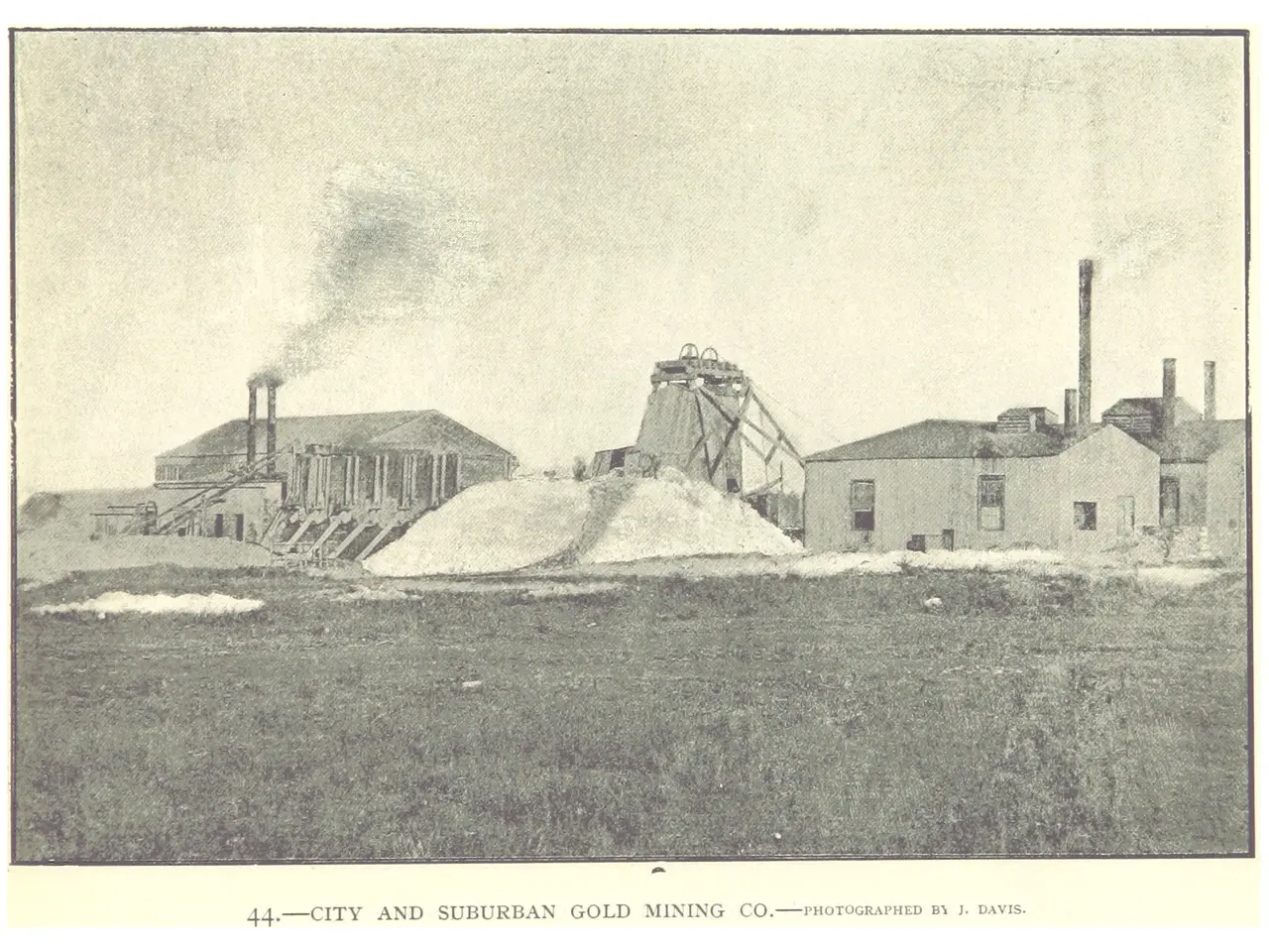 The image shows a black and white photo of a city and suburban gold mining company, with buildings,...