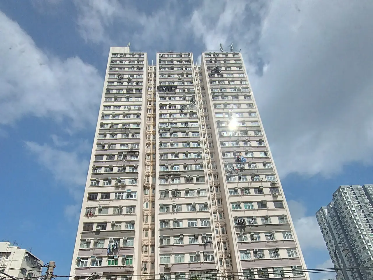 The image shows a tall apartment building in the middle of a bustling city street, surrounded by...