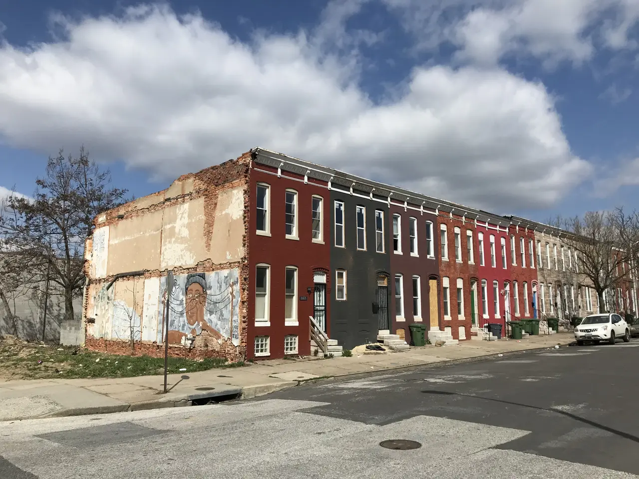 The image shows a row of houses on the corner of a street, with windows, doors, steps, railings,...