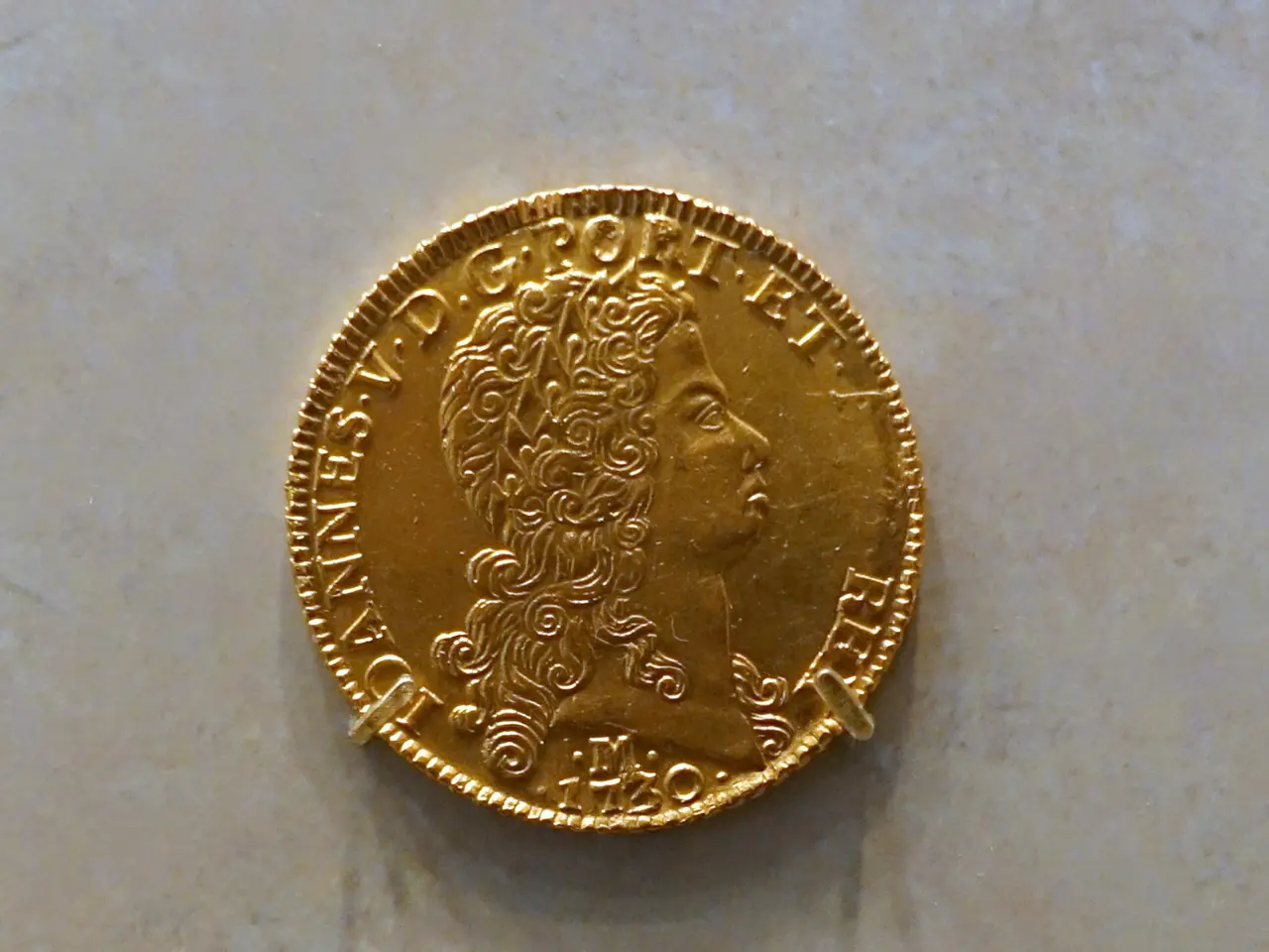 The image shows a gold coin on display in a museum, with the text "Brazil 12,800 Reis 1730"...