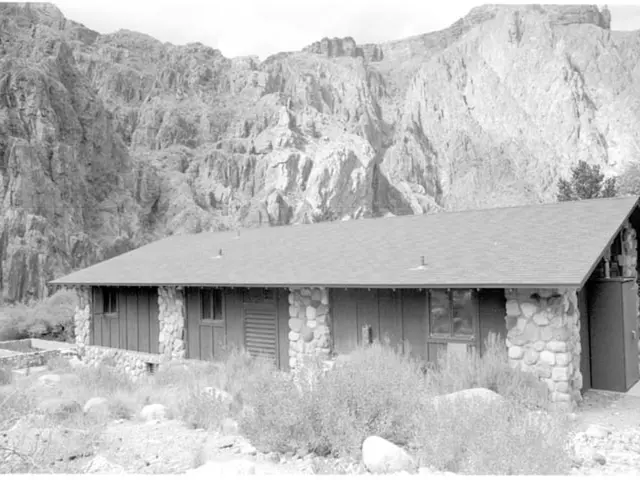 In this image in the front there are stones and there is grass. In the center there is a cottage....