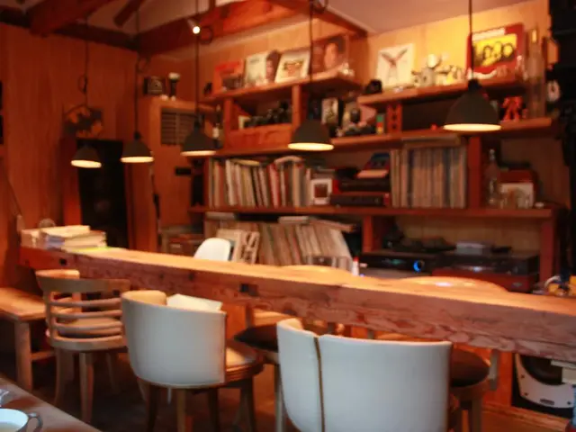 In the middle there is a bookshelf ,lights and wall. On the left there are three chairs and table....