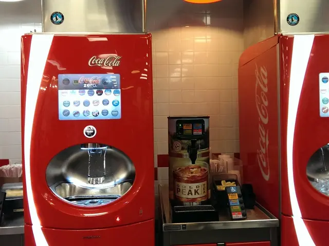 In this image we can see coke machines. In the background of the image there is wall.