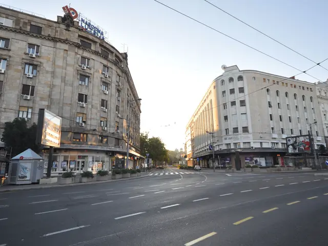 Here we can see buildings with windows. In-front of these buildings there are hoarding, trees and...