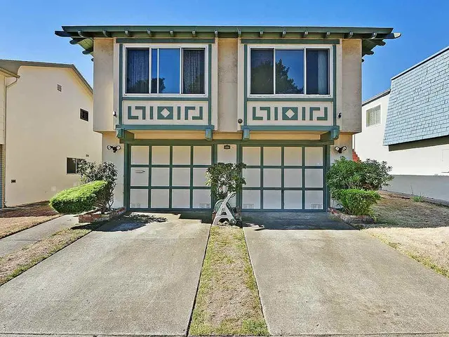 The image shows a two story house with a driveway in front of it, surrounded by lush green grass...