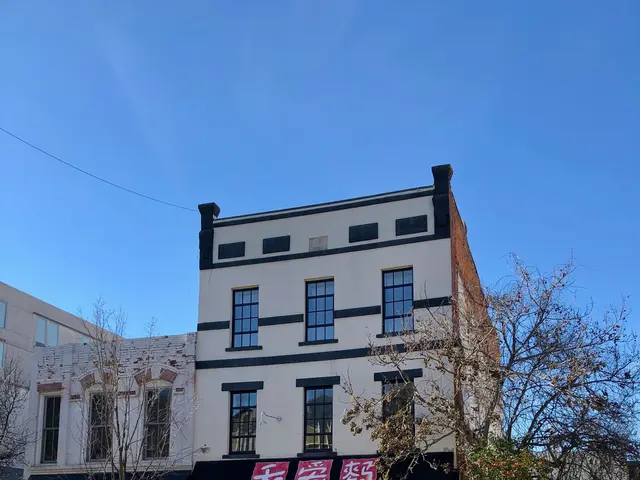 The image shows a street corner with cars parked on the side of it, buildings with windows, trees,...