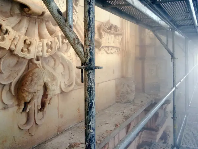 The image shows a building with a wall featuring intricate carvings on the left side, metal rods on...