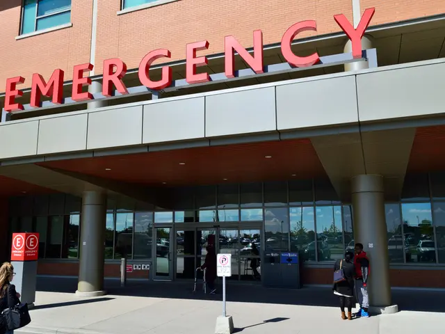 The image shows a group of people walking in front of an emergency building with glass walls and...