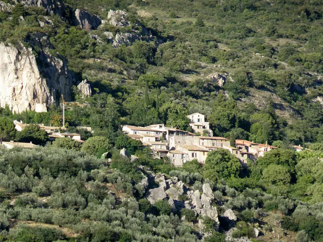The image shows a small village nestled in the middle of a mountain, surrounded by trees and...