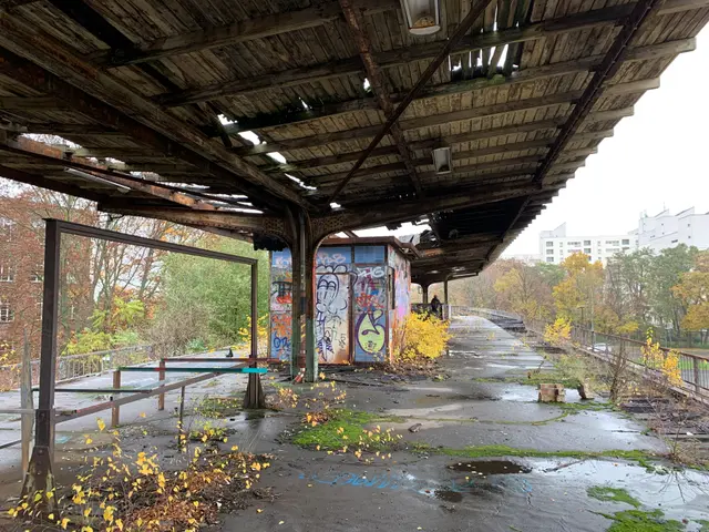 The image shows an abandoned train station with graffiti on the side of it. Underneath the bridge,...