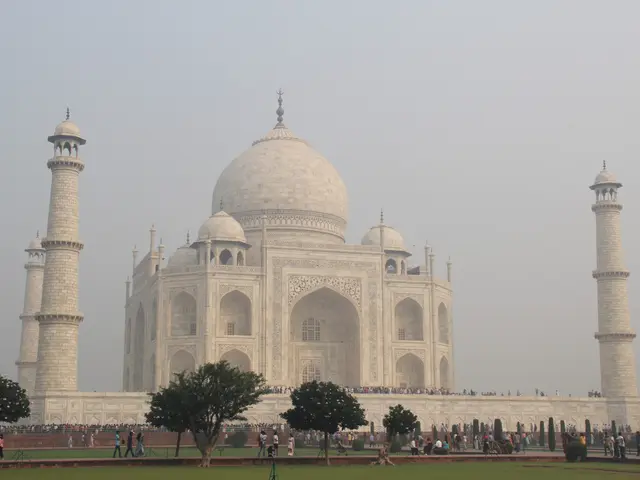 The image shows the majestic Taj Mahal in Agra, India, surrounded by lush green grass, trees, and...