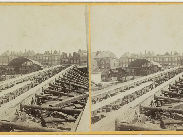 The image shows an old black and white photo of a train track with buildings in the background. On...