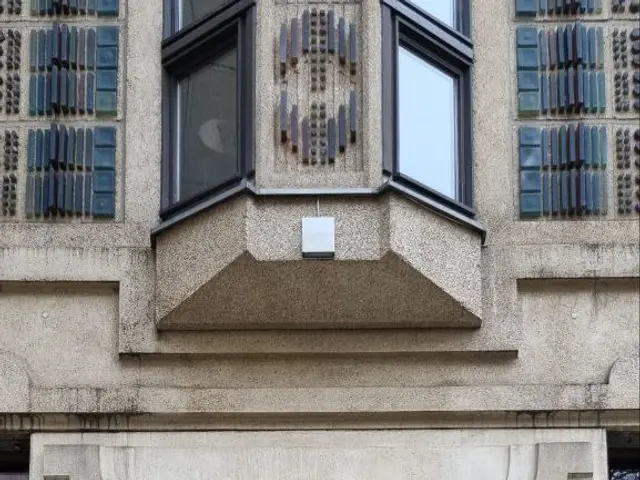 The image shows a building with glass windows and a decorative design on the side of it. At the...