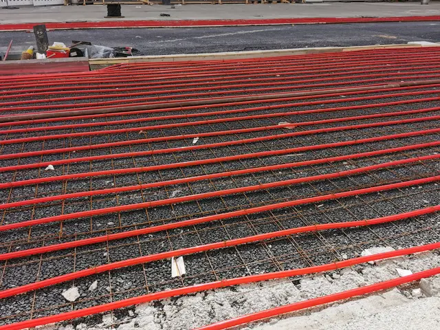 The image shows a construction site with a large pile of red pipes on the ground, surrounded by...