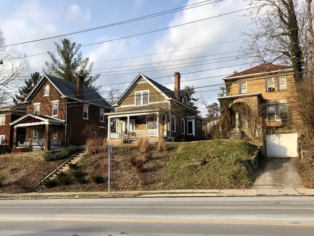 The image shows a row of houses sitting on the side of a road, with windows, doors, pillars,...