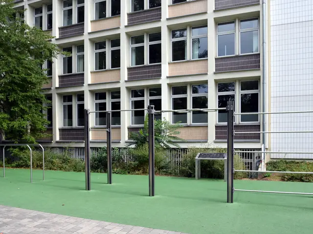 The image shows a building with windows, railings and balconies, surrounded by plants, trees and...