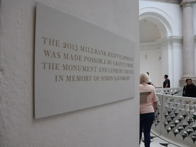 The image shows a group of people standing on the floor of a building, with a board on the wall...